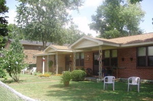 Shows the front yard and entrance to a single story, brick, duplex style rowhouse